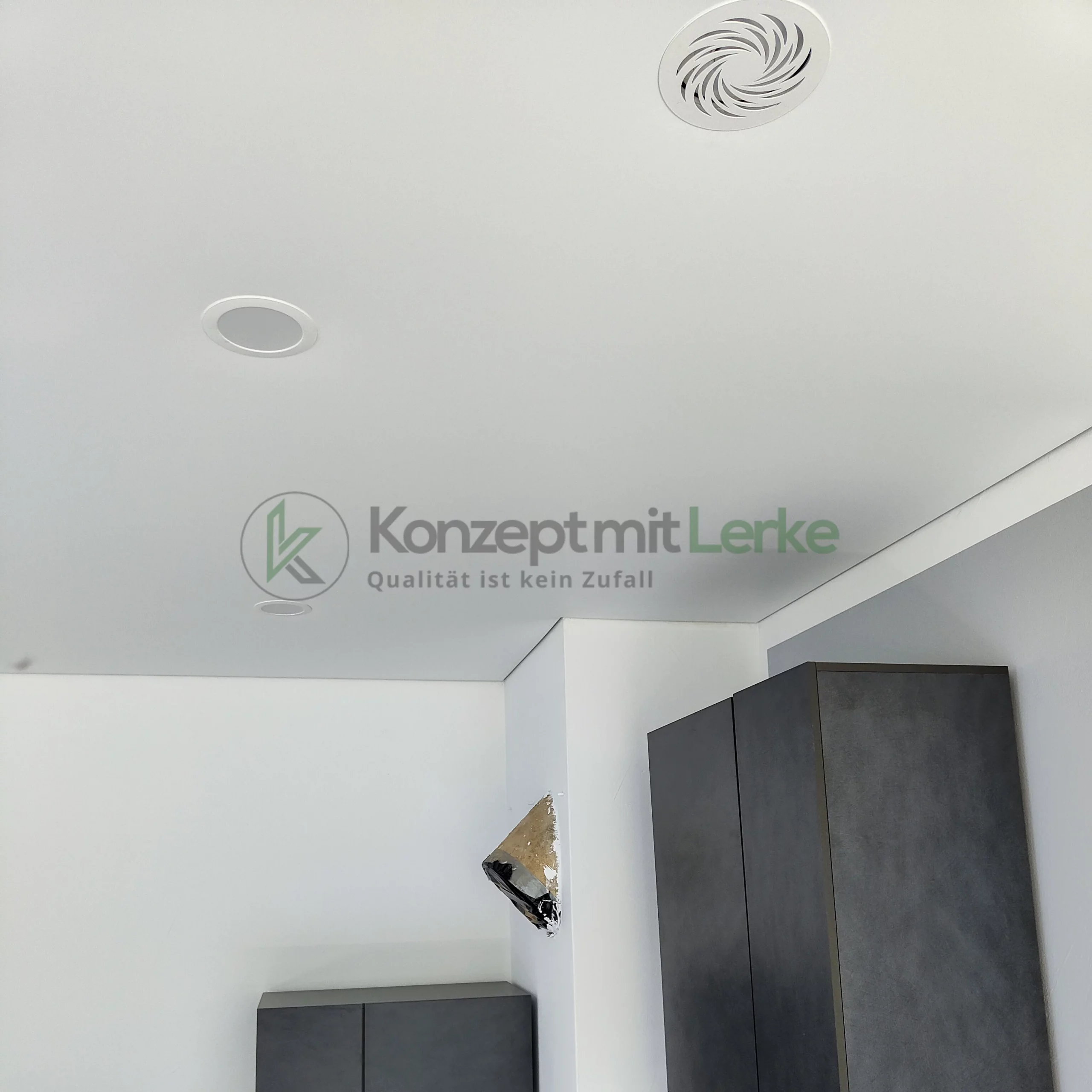 Weiße matte Spanndecke mit runden Einbauspots und integriertem Lüftungsgitter über einem modern eingerichteten Wohnbereich.